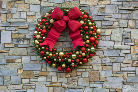 Christmas Holiday Wreath with red bow ribbons ornaments hanging on rock stone wallの写真素材