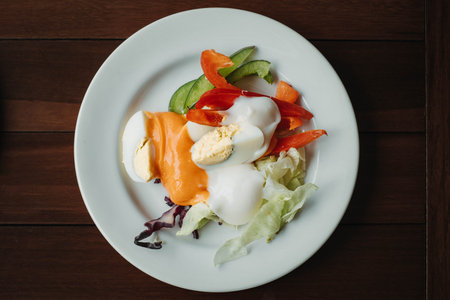 Flat lay or top view shot of a plate of salad consisting of tomatoes, peppers, cabbage, purple cabbage and eggs topped with peanut sauce served on a white plate in the wooden tableの写真素材