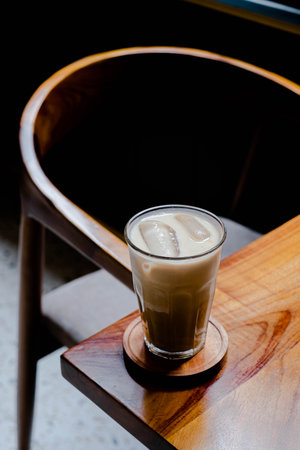 Hi-res photo of vertical shot of a glass of iced coffee latte in a wooden coaster and table with blurred background, narrow depth of fieldの写真素材