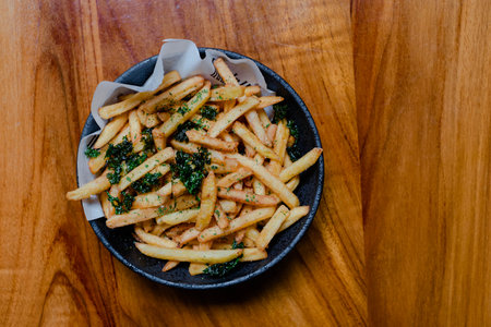 Hi-res photo of flat lay or top view shot of a bowl of French Fries with some vegetables topping in...
