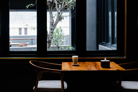Hi-res photo of an empty chair with a glass of iced coffee latte in the wooden table, narrow depth...