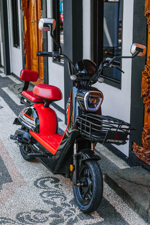 A black and red electric bike with basket in the front of it is parked in the front of a cottage's door roomのeditorial素材