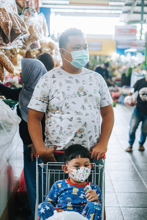 An Indonesian father is pushing shopping car while his kid is sitting on itのeditorial素材