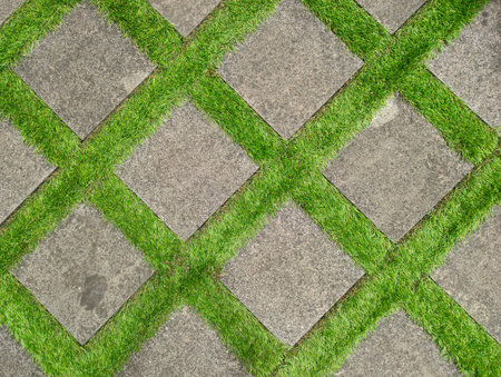 Flat lay shot of tile pavement close-up with artificial green grass diagonal. Abstract background texture.の写真素材