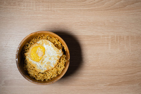 Flat Lay of Fried Noodles and Sunny-Side Up Egg on a Wooden Bowl and Wooden Tableの写真素材