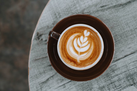 Flat lay or top view shot of a cup of coffee with beautiful Latte Art on wooden table. Blurred background.の写真素材