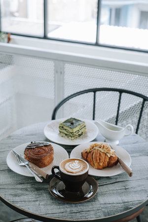 A table with plates of bakery and cups of coffee on it. Focused on the cup of coffee. Portrait or vertical. Morning breakfast. Blurred background.の写真素材