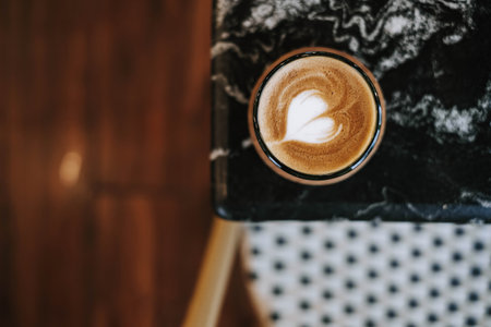 Flat lay or top view shot of a cup of coffee with beautiful and simple Latte Art on black marble table. Blurred background.の写真素材