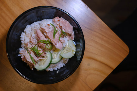 Flat lay or top view shot of a bowl of Steamed Chicken with Rice, Vegetables, and some Cucumbers on a wooden tableの写真素材