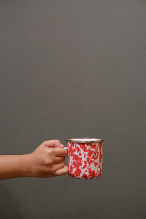 Portrait or vertical shot of a handheld vintage enamel mug on a dark grey backgroundの写真素材
