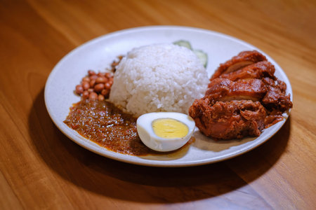 A plate of Nasi Lemak containing Crispy Chicken, Egg, Peanuts, Lemak Sauce, and Anchovy fish with blurred backgroundの写真素材