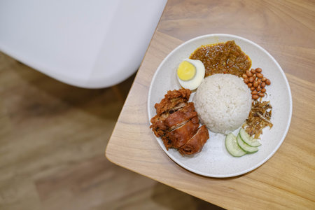 Flat lay or top view shot of a plate of Nasi Lemak containing Crispy Chicken, Egg, Peanuts, Lemak Sauce, and Anchovy fishの写真素材