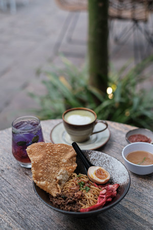 Portrait or vertical shot of a bowl of Fried Chinese Noodles with Shredded Chicken, Char Siu, a Half-Boiled Egg, and a Fried Dumpling on the wooden table with blurred background. Soft focus or unfocused.の写真素材