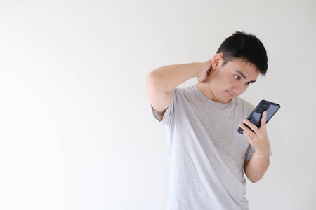Medium and soft-focused shot of a young Asian man who wears a grey t-shirt and is shocked while...