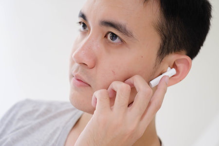 Close-up shot of the partial face of a young Asian man listening to white true wireless stereo earphones. Focus on the eye. Unfocused or shallow depth-of-field. Isolated white background.の写真素材