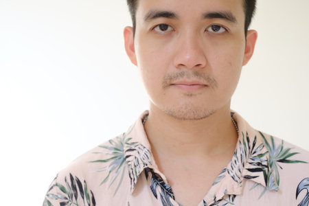 Close-up shot of a young Asian man wearing a pink shirt with tropical patterns is looking at the camera. Isolated white background.の写真素材