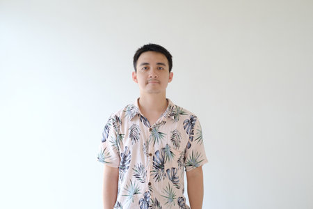 A young Asian man wearing a pink shirt with tropical patterns is standing and looking at the camera. Isolated white background.の写真素材