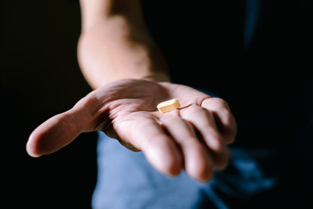 A yellow pill on a hand palm with silhouette. Isolated black background. Soft focus or unfocused. Suitable for advertisement.の写真素材