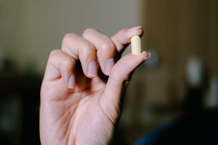 A yellow pill is held by pointing and thumb fingers with three other fingers are down. Isolated black background. Suitable for advertisement.の写真素材