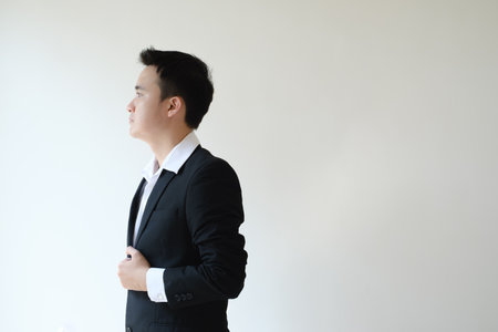 A young Asian businessman wearing a white shirt with a black suit is standing and looking at the right side. Isolated white background.の写真素材