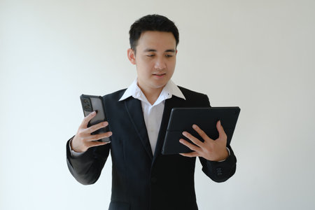 Young Asian business man holding a smartphone and a tablet device and looking at it. Isolated white...