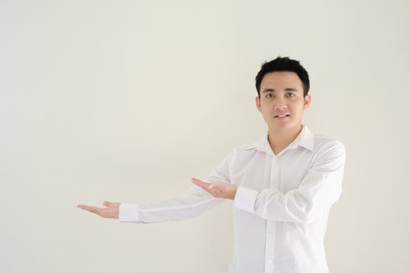 Young Asian man wearing a white shirt opening his right hand to his right side and looking at it. Isolated white background.の写真素材