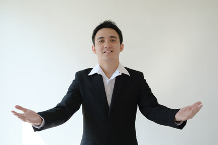 A young Asian businessman wearing a black suit and a white shirt with a smile face expression and both hands open. Isolated white background.の写真素材