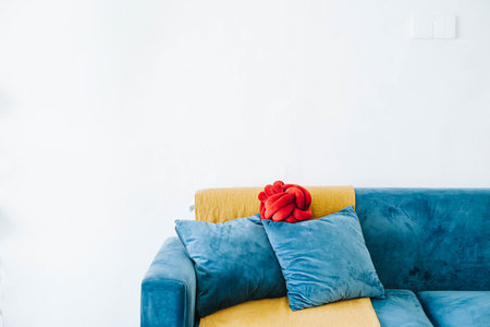 Blue sofa, 2 solid filled cushion, and a red cushion with a golden throw against white wall as backgroundの写真素材