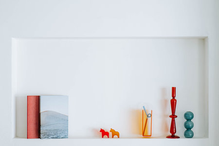 Books and miscellaneous decorations on white nook wall which functions as a shelfの素材 [FY310211024247]