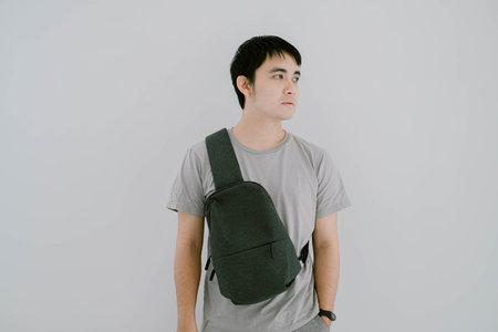 Selective focus shot of young Asian man wearing sage green casual T-Shirt and minimalist sling bag is looking at the right sideの写真素材