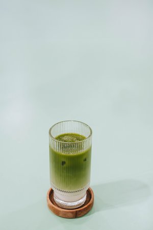 Portrait or vertical and selective focus shot of a glass of Ice Matcha or Japanese Green Tea Latte on wooden coaster on isolated sage green pastel tableの写真素材