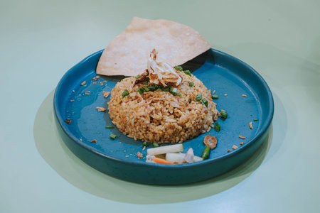 Selective shot of a plate of Nasi Goreng or Fried Rice with cracker, carrots, and cucumber on isolated sage green pastel backgroundの写真素材