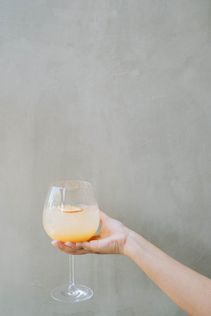 Portrait or vertical and selective focus shot of a hand holding an Ice Tropical Sangria or Orange Cocktail with Soda on the wine glass isolated on grey backgroundの写真素材