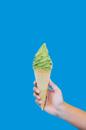 Matcha Ice Cream Cone is held by hand on isolated blue backgroundの写真素材