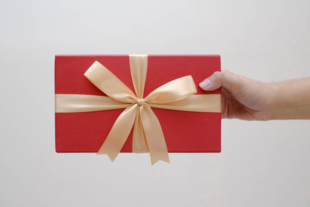Male hands holding a small red gift box wrapped with gold ribbon. Isolated white background....