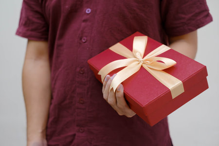 Male hands holding a small red gift box wrapped with gold ribbon. Close up and indoor shot....