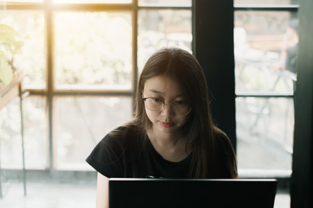 Young Asian woman wearing casual outfit working on a laptop in an industrial room or cafeの写真素材