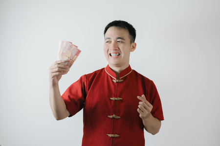 Smile face expression of Asian man wearing Cheongsam or traditional costume while holding amounts of money on white background. Chinese New Year concept.の写真素材