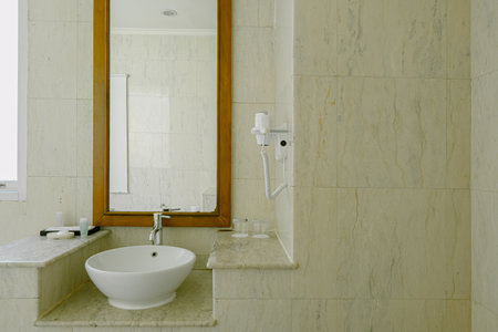Luxury bathroom with a white ceramic sink, faucet, and a mirror with a shelf above it. A hairdryer is placed on the shelf. Clean, classic, and well-maintained interior.の写真素材