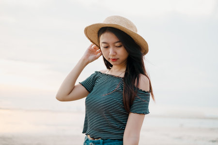 A beautiful young Asian girl on the beach during sunset with bokeh background. The girl wearing straw hat.の写真素材