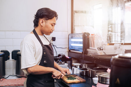 A Southeast Asian chef with an apron chops the leeks on a wooden cutting board in the kitchen in the afternoon with bokeh backgroundの写真素材