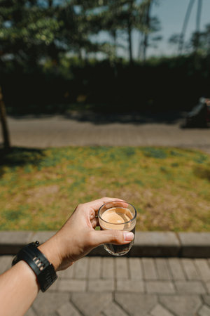 A hand holding a glass of single-shot espresso in the morning on the paved sidewalk streetの写真素材