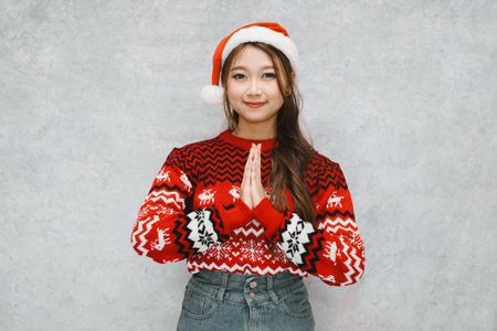 Smile face of a young Asian Santa woman with greeting or namaste gesture. Suitable for promotional material during holiday season.の写真素材