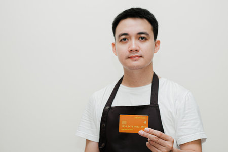 Young Asian chef holding a credit card while looking at the camera. Isolated background.の写真素材