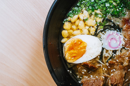 Flat lay photo of Japanese Ramen with corn, leeks, half of an egg, beef, nori, and narutomaki. Chopsticks on the black bowl.の写真素材