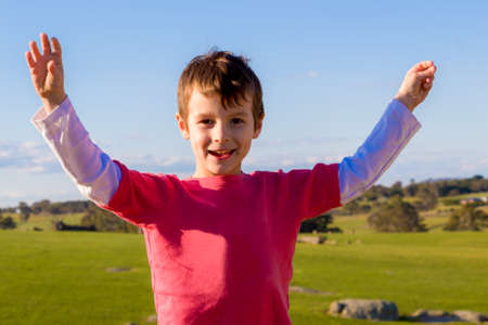 Happy boy with arms up standing in a green field.の写真素材