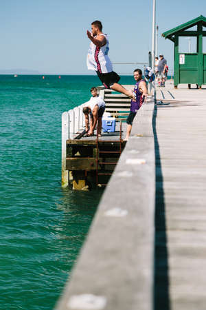 MELBOURNE/AUSTRALIA - FEBRUARY 6: Youths jump off a jetty into the water, while others fish in Mordialloc, a coastal suburb of Melbourne, Australia in February.の写真素材