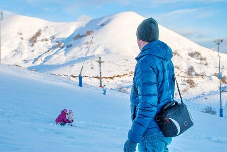Father turned to hail daughter, next to which sits mother on a ski slope in the mountains