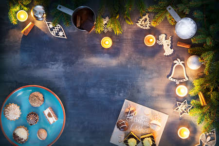 Christmas table with sweets, burning candles, christmas ornaments, ingredients and tree branches on the gray wooden tableの写真素材