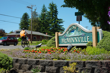 MCMINNVILLE, OREGON JUNE 6TH 2017, A roadside sign welcoming people to the city of McMinnville surrounded by planted flowers. A car and a bicyclist are going by.のeditorial素材